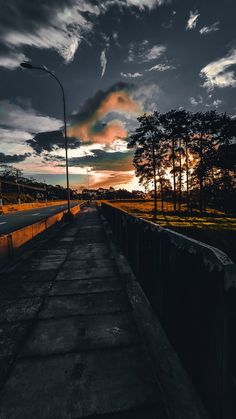 the sun is setting behind some trees on the side of an empty road with no cars