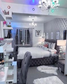 a bedroom decorated in gray and white with chandelier, bed, desk, chair, mirror