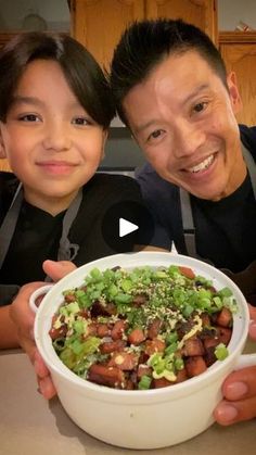 the man and child are holding up a bowl full of food with vegetables in it