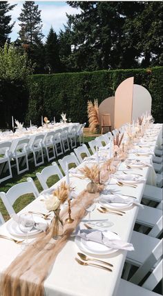 a long table is set with white plates and silverware for an outdoor wedding reception