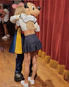 two people are hugging each other in front of a mickey mouse mascot and red curtains