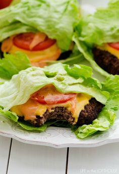 three hamburgers with lettuce and tomatoes on them sitting on a white plate