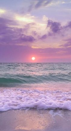 the sun is setting over the ocean with waves coming in to shore and purple clouds