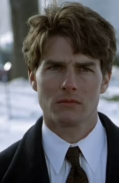 a man in a suit and tie looking at the camera with snow on the ground behind him