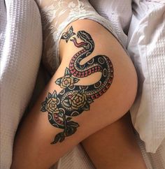 a woman laying in bed with a snake tattoo on her thigh and leg next to a pillow