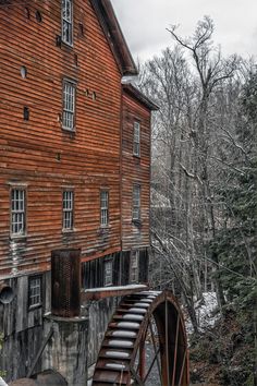 an old wooden building with a water wheel next to it and trees in the background