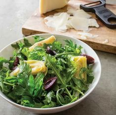 a white bowl filled with greens and cheese next to a knife on a cutting board