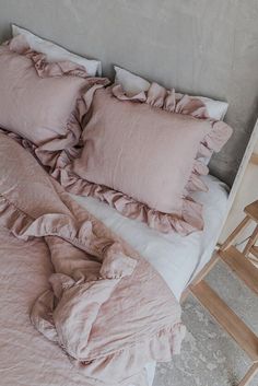 an unmade bed with pink sheets and ruffles on the pillowcase, next to a wooden chair