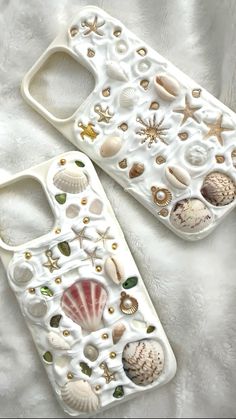 two cell phones with shells and seashells on them sitting on a white blanket