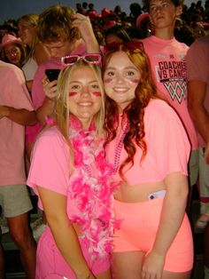 two young women in pink outfits posing for the camera with other people behind them at a sporting event