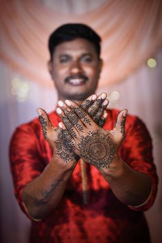 a man is holding his hands up with hendi tattoos on their palms and smiling at the camera