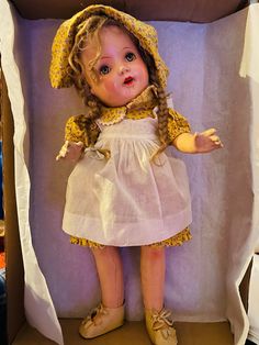 a doll in a cardboard box with clothes and shoes on it's feet, wearing a bonnet