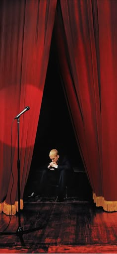 a man sitting in front of a red curtain with a microphone next to his head