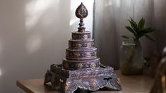 an ornate metal object on a table next to a vase with a plant in it