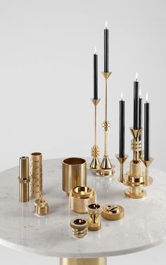 an assortment of brass candle holders and candles on a white marble table with gold accents