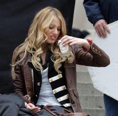 a woman sitting on the ground with a handbag and coffee cup in her hand