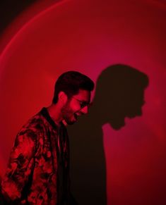 a man standing in front of a red light with his shadow on the wall behind him