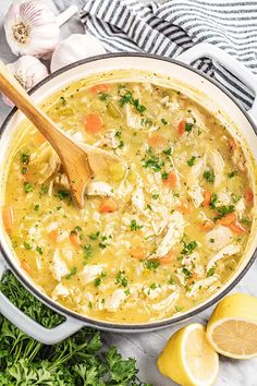 a pot filled with chicken and rice soup next to lemons, parsley and garlic