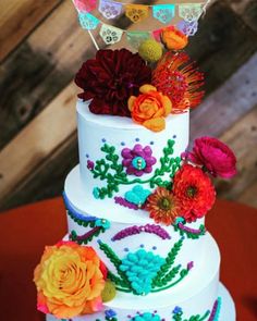 a three tiered cake decorated with flowers and bunting on the top is sitting on a red tablecloth