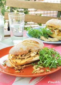 two plates with sandwiches on them sitting on a patio table next to a glass of water