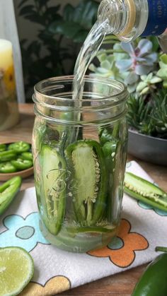 a jar filled with cucumbers sitting on top of a table next to other vegetables