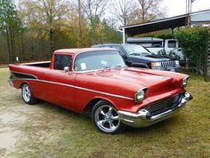 an old red car is parked in the grass