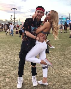 a man and woman hugging each other in the middle of a field at an outdoor music festival