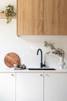 a white kitchen with wooden cabinets and black faucet in the center, along with a cutting board on the counter