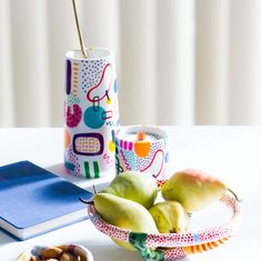 some fruit is sitting on a table next to a book and a cup with a straw in it