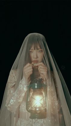 a woman wearing a veil and holding a lantern in her hands with the light shining on her face