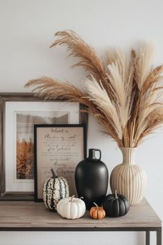 there is a vase with some plants in it and two pumpkins on the table