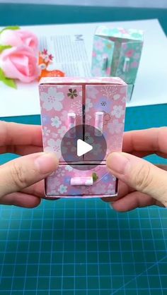 someone is holding up a pink box with flowers on it, and the video appears to be playing