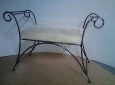 a wrought iron bench with a white cushion on it's back rests against a wall