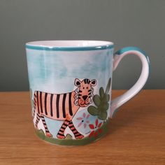 a coffee cup with a zebra painted on the front and side, sitting on a wooden table