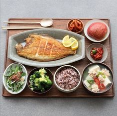 a wooden tray topped with different types of food and bowls filled with meat, veggies and sauces