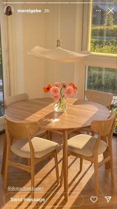 a wooden table and chairs with flowers in a vase on the table next to a window