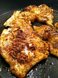 two pieces of chicken in a frying pan with some seasoning on them and one piece being fried