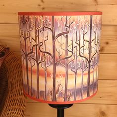 a lamp on a table next to a basket and tree wallpapered lampshade