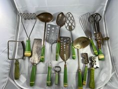 an assortment of kitchen utensils in a white box with green handles and spoons