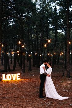 a bride and groom are standing in the woods with lights strung from trees above them