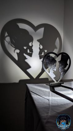 the shadow of two people in front of a heart on a table with a black cloth