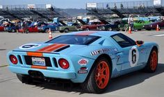 a blue sports car with orange rims parked in a parking lot next to other cars