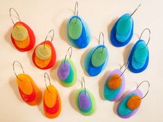 there are many different shapes and sizes of earrings hanging on the wall, one is orange, blue, green, yellow, and red