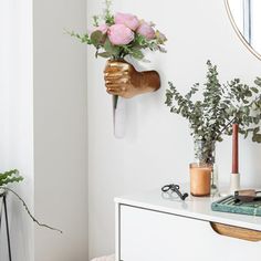 a white dresser topped with vases filled with flowers and greenery next to a mirror