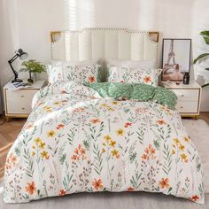 a bed with flowers on it in a room next to a dresser and lamp stand