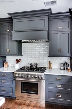 a stove top oven sitting inside of a kitchen next to gray cabinets and white counter tops