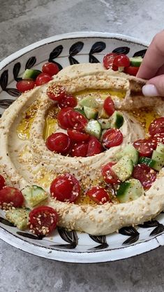 a plate with hummus, tomatoes and cucumbers on it is being held by a hand