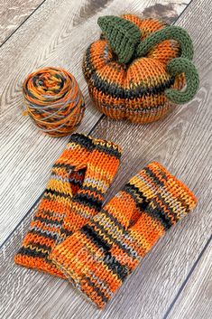 two knitted pumpkins sitting on top of a wooden floor next to some yarn