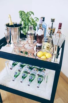 a bar cart filled with liquor bottles and glasses on top of a wooden floor next to a potted plant