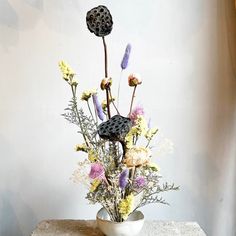 a white vase filled with lots of flowers on top of a wooden table next to a wall